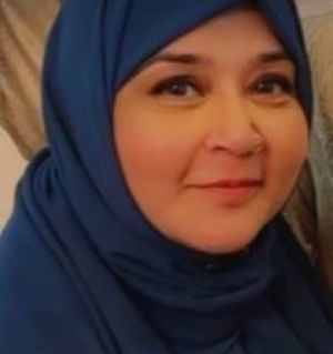 Photo of Azra. Azra is looking sideways at the camera and smiling discreetly. She is wearing a navy blue hijab.