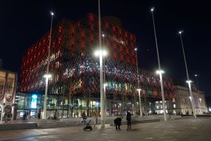 External view of the Library of Birmingham covered in red lighting. The photo has bee taken at night, it is dark and the library is surrounded by bright streetlighting.